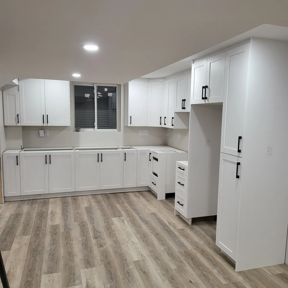 Finished basement kitchenette with white shaker cabinetry, black hardware, quartz counter and vinyl plank flooring