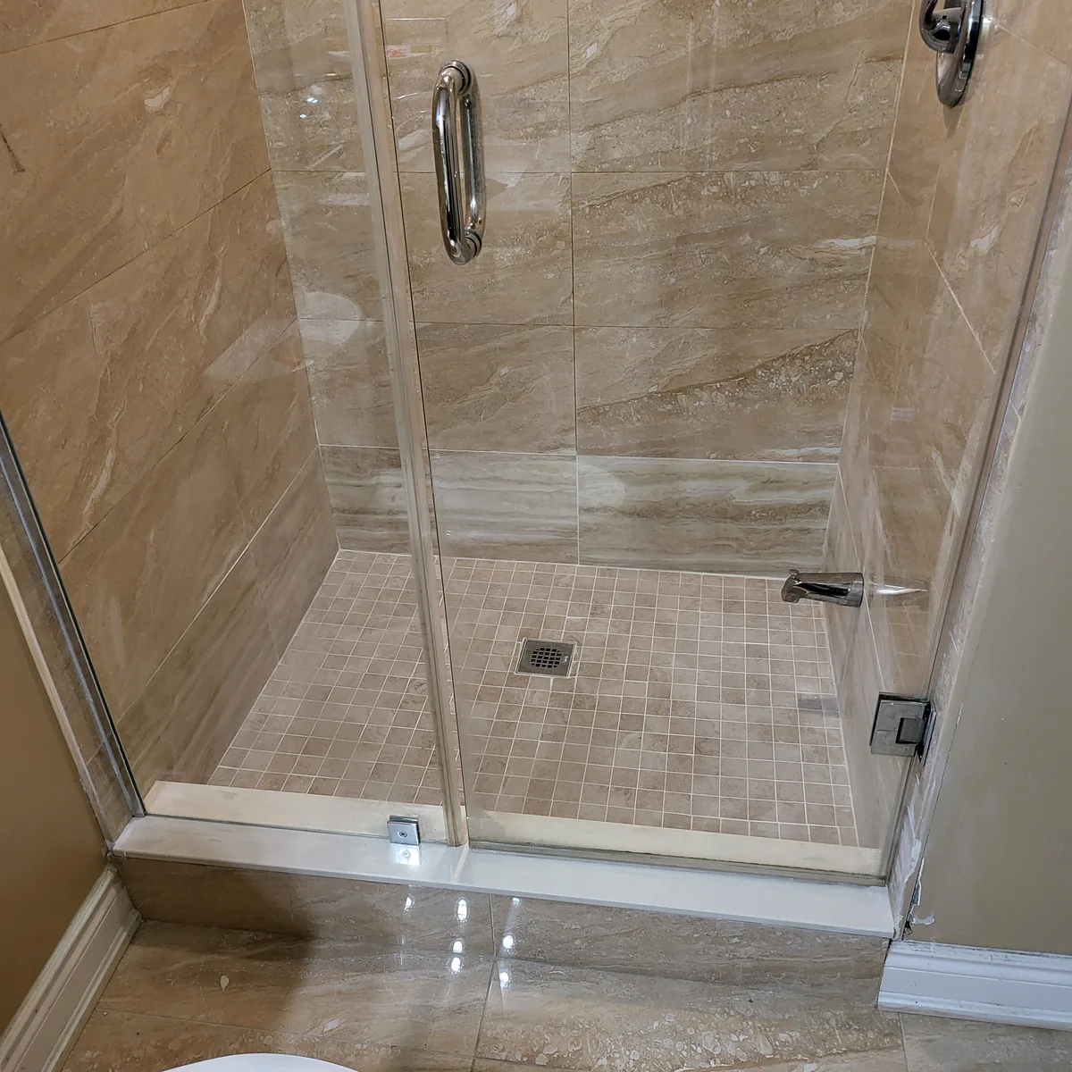 Completed bathroom shower in stone-look porcelain with a mosaic floor, chrome fixtures and a framed glass enclosure