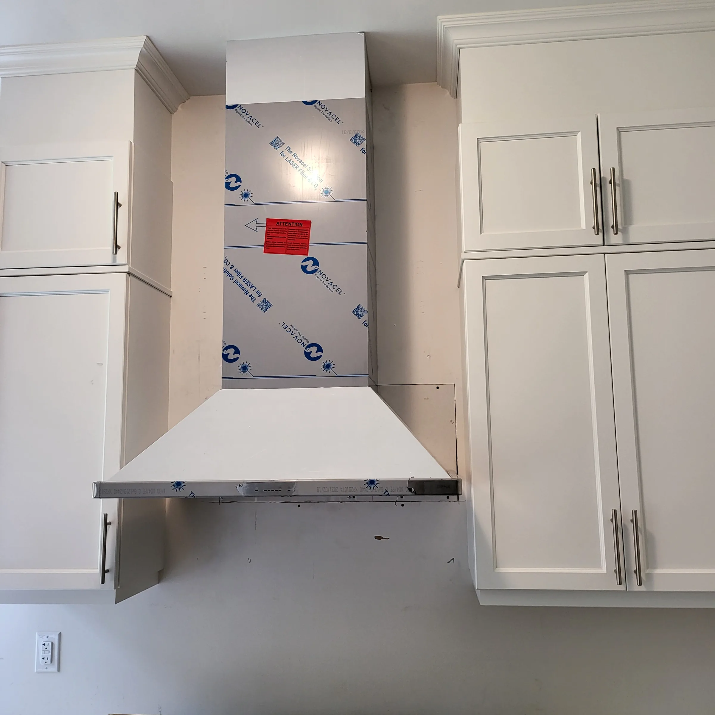 Custom range hood surround framed and clad between upper cabinets, with the protective film still on the hood