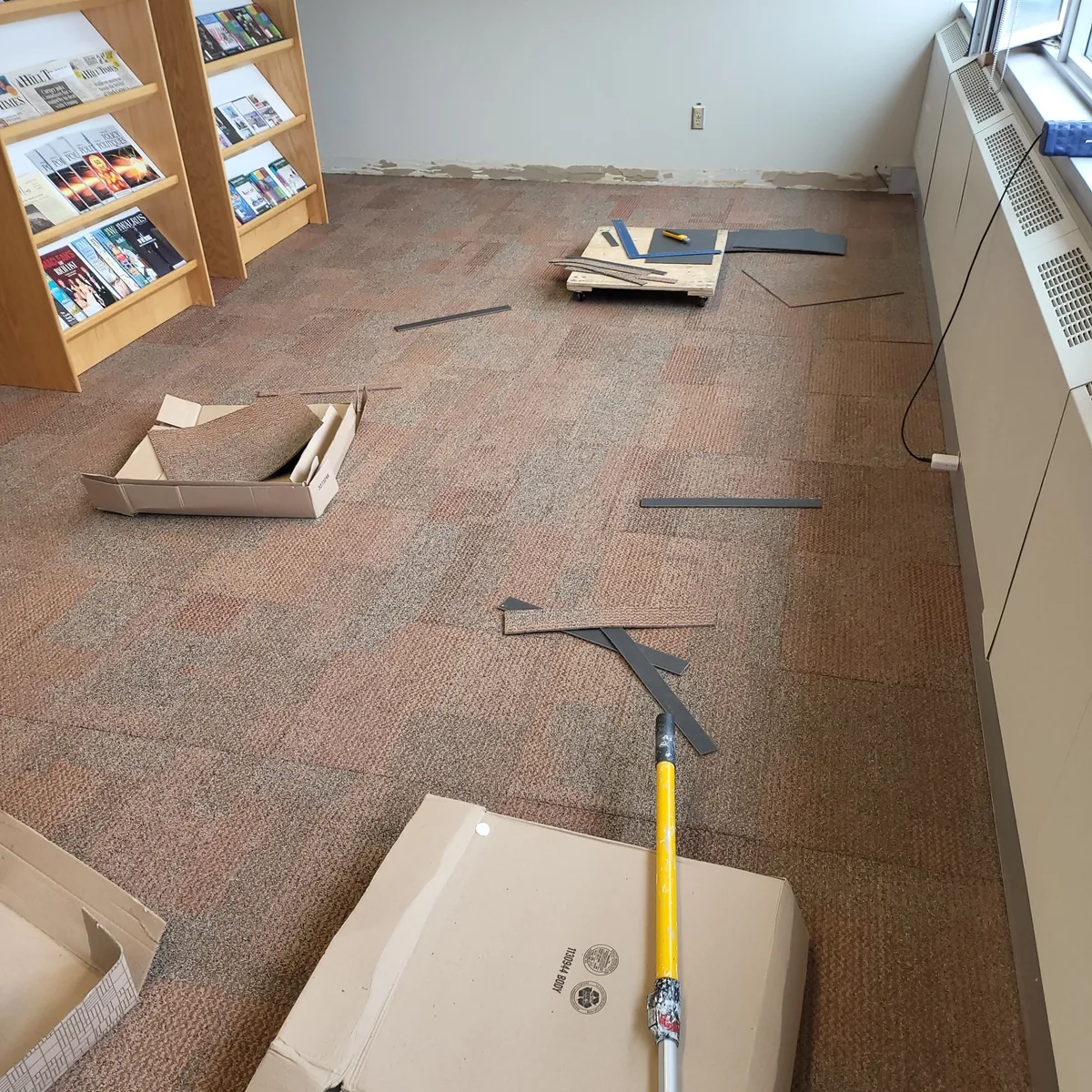 Carpet tile being laid in a commercial office, with display shelving along one wall